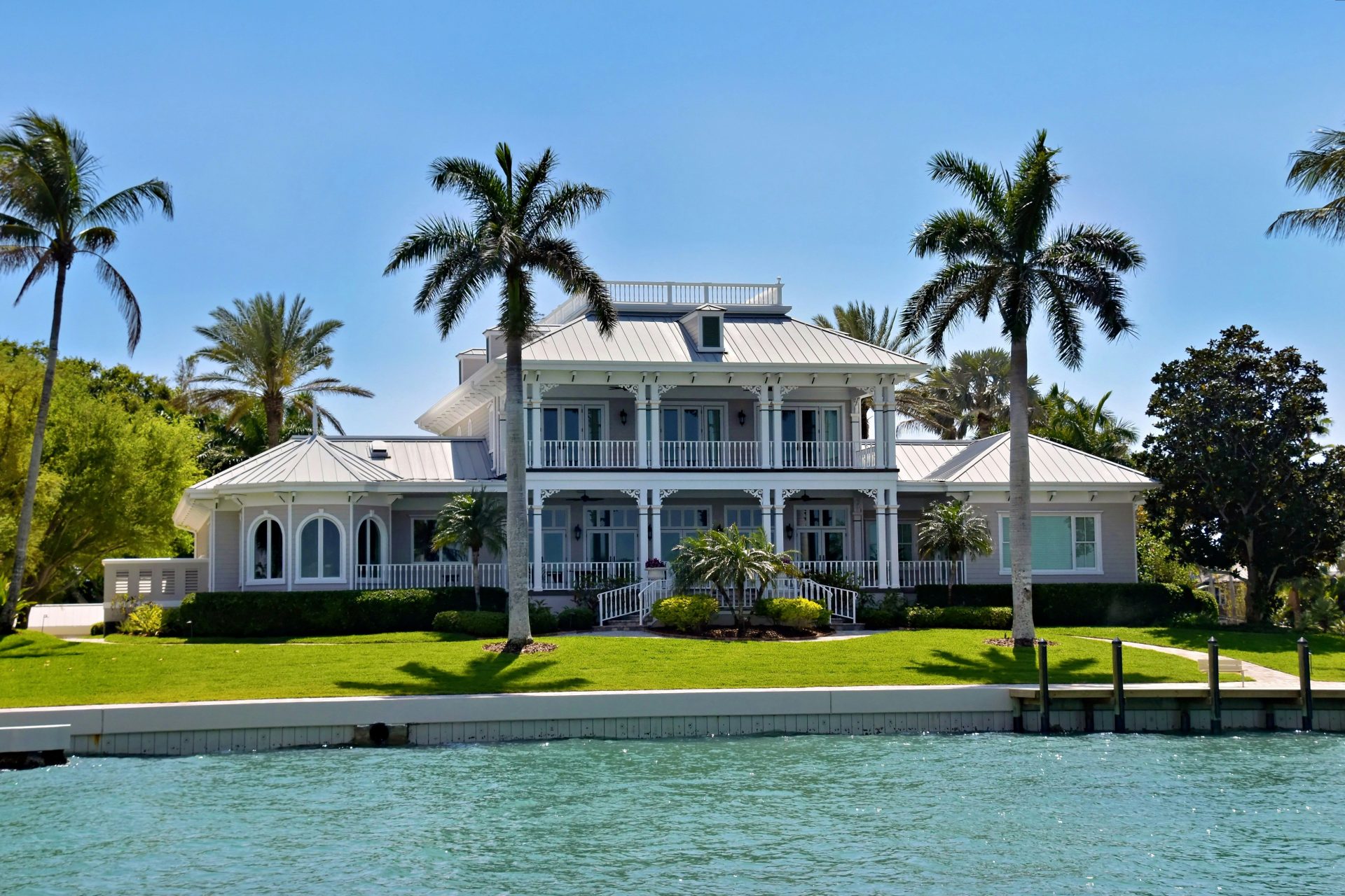 A large white house with palm trees by the water.